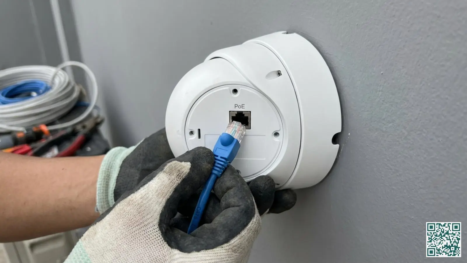 Handen sluiten een blauwe CAT6 netwerkkabel aan op de achterkant van een witte dome beveiligingscamera via PoE